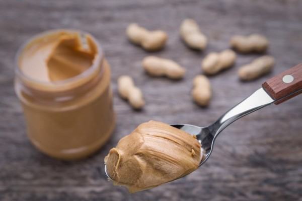 Peanut cream in spoon. Against the background of nuts and container.